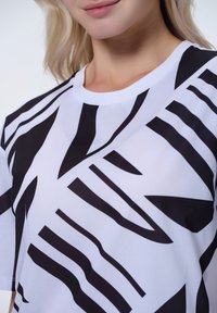 T-shirt bianco con audaci strisce e forme astratte nere. Collo rotondo e maniche corte, realizzato in morbido cotone.
