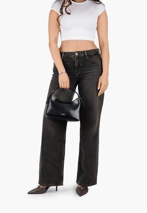 Woman wearing white crop top and black high-waist wide-leg jeans holding a black leather handbag, wearing black pointed heels.