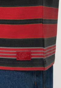 Κόκκινη και γκρι ριγωτή μπλούζα από ύφασμα με ζωντανό μπαλώμα που φέρει το λογότυπο "Vans" στο τελείωμα. Μαλακή πλεκτή υφή με αντίθετα χρώματα για τονισμούς.