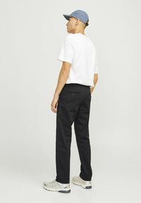 Schwarze Hose mit entspanntem Schnitt, kombiniert mit einem weißen T-Shirt und einer blauen Mütze. Verfügt über eine Gesäßtasche mit Knopfdetails.