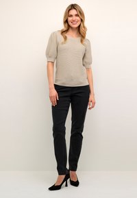 Světlé šedé, dobře padnoucí halenka s nafouknutými rukávy, spárovaná s černými slim-fit džíny a černými vysokými podpatky, na neutrálním pozadí.