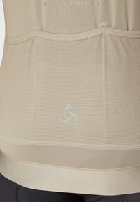 Beige atletisk skjorte med et teksturert strikkemønster, som har subtil merking og en jevn kant, designet for komfort og ytelse.
