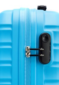 Valigia rigida blu chiaro con superficie testurizzata, zip in metallo e un lucchetto a combinazione nero di lato.