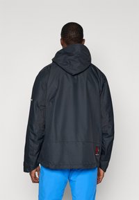 Musthave must, millel koos kapuutsiga, tekstureeritud hallide külgpaneelidega ja logoplaadiga alumisel seljal. Peenike ja kergesti kantav disain.