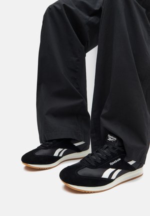 Černé tenisky s vrškem ze semiše a síťoviny, s bílými pruhy a logem Reebok. Tvarované v klasickém atletickém stylu s gumovou podrážkou.