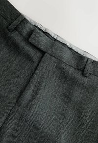 Gray herringbone trousers featuring a smooth waistband with a subtle sheen and tailored pleats for added shape and dimension.