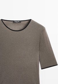 Korte mouwen, olijfgroen T-shirt met een ronde halslijn afgewerkt met zwart. Zacht materiaal met een gladde textuur. Logo-label bevindt zich bij de halslijn.