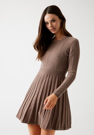 Vestito in maglia marrone con texture a coste, maniche lunghe e gonna plissettata svasata. Bustino aderente che si trasforma in una gonna fluida.