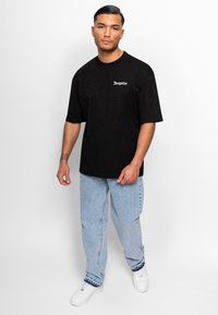 Sort t-shirt med korte ærmer og "Dropsize" logo i hvid; parret med lyseblå løstsiddende jeans og hvide sneakers.