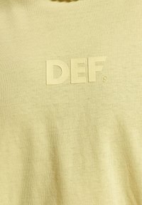Koszulka z krótkim rękawem w jasny żółtym kolorze z wypukłym logo „DEF”. Miękka tkanina o gładkiej strukturze i prostym fasonie.