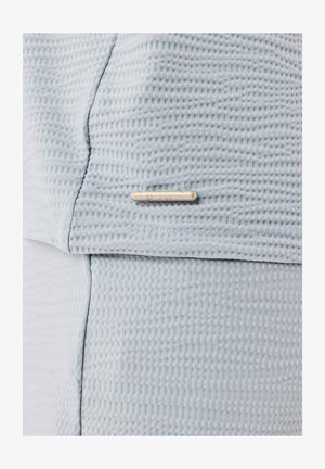 Lichtblauwe textuurstof met een subtiel patroon, met een klein metalen labelaccent nabij de naad. Het materiaal lijkt zacht en ademend.