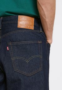 Dark blue denim jeans with a leather back patch. Features yellow stitching and a small red Levi's tab on the back pocket.