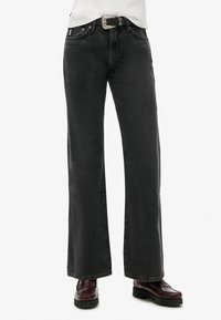 Jeans de mezclilla negros de pierna ancha con una textura ligeramente descolorida, cinco bolsillos, herrajes metálicos y un cinturón negro con una hebilla plateada.