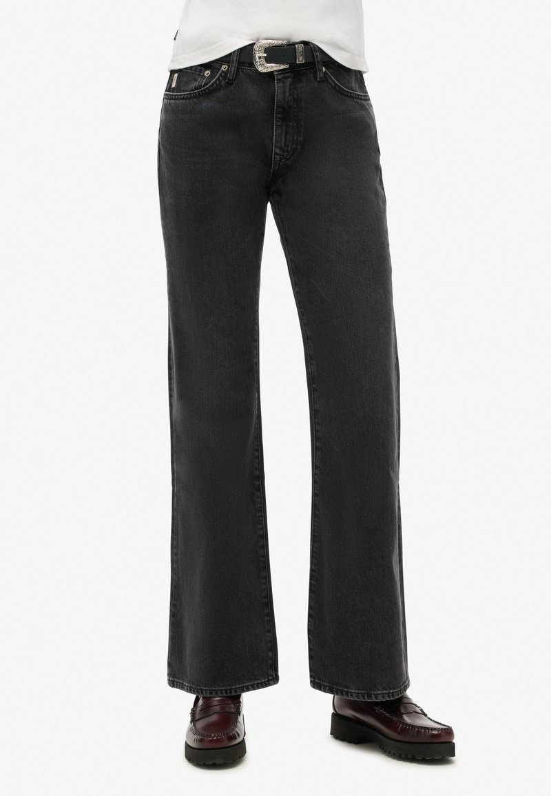 Jeans de mezclilla negros de pierna ancha con una textura ligeramente descolorida, cinco bolsillos, herrajes metálicos y un cinturón negro con una hebilla plateada.