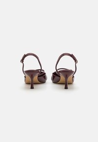 Talons en cuir verni bordeaux avec une pointe ronde, une fine sangle à la cheville et un talon stiletto de 5 cm. Fini lisse avec un subtil détail de couture.