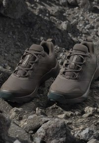 Brązowe buty do biegania trail Adidas Terrex umieszczone na skalistym terenie na zewnątrz.
