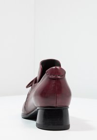 Chaussure en cuir bordeaux avec une bout arrondi, un petit talon noir, et une couture le long du talon. Le design comporte un accent de nœud décoratif.