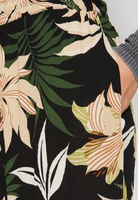 Tissu noir présentant de grands motifs floraux en tons verts, crème et pêche. Accentué par des détails rayés et une finition texturée.