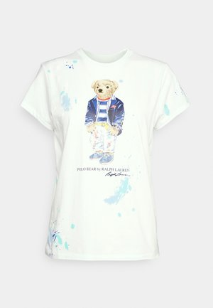 Biała koszulka z grafiką stojącego misia w niebieskiej kurtce, paskowanej koszuli, białych spodniach i trampkach, z napisem "Polo Bear by Ralph Lauren".