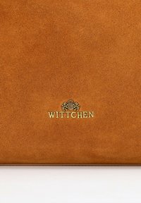 Brązowa torebka z zamszu o gładkiej fakturze, z wygrawerowanym złotym logo z przodu. Prosty, prostokątny kształt, bez dodatkowych akcentów.