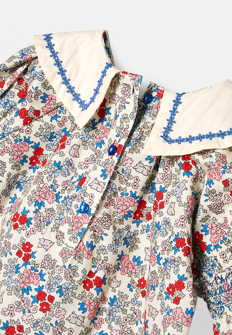Blumengemustertes Kleid in Beige, mit roten, blauen und pinken Blumen. Großer weißer Kragen mit blauer Stickerei und blauen Knöpfen.