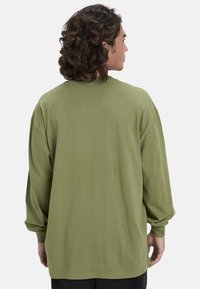 Langarmshirt aus olivgrüner Baumwolle. Verfügt über eine lockere Passform, einen runden Ausschnitt und überschnittene Schultern. Glatte Textur, minimalistische Details.