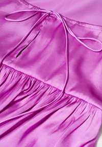 Section de robe en satin rose avec un tissu froncé à la taille et un lien en ruban. Texture lisse avec un léger éclat, présentant une petite ouverture.