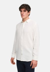Witte langemouwen overhemd van gestructureerde katoenstof, met een button-down kraag en een voorpand met knopen, gedragen met donkere broeken.