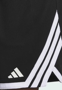 Pantalones cortos deportivos negros hechos de un material de malla transpirable. Presentan tres rayas blancas en los laterales y un logo blanco de Adidas cerca del dobladillo.