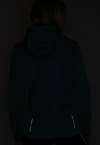 Donkergroene, lichte hoodiejack met een slim-fit ontwerp, voorzien van reflecterende accenten bij de zoom en manchetten. Vloeiende textuur, minimale details.