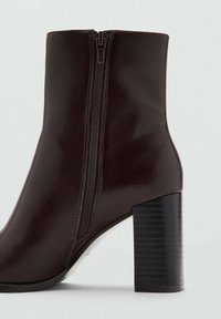 Bottine en cuir marron avec une fermeture éclair latérale, un bout carré et un talon bloc noir rainuré. Texture polie et design épuré.