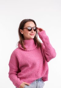 Růžový pletený svetr s vysokým límcem, který má vroubkovanou strukturu. Kolo brýle z želvoviny dotvářejí vzhled. Ležérní džíny kraťasy dokončují outfit.