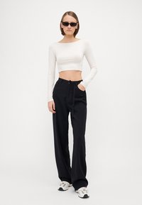 Svarte vid legged bukser med knyteliv, kombinert med en tettsittende hvit kort topp. Modellen har på seg svarte solbriller og hvite joggesko.