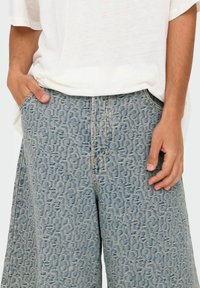 Shorts de mezclilla con un lavado azul claro y un patrón en relieve, con bolsillos laterales y un corte relajado, combinados con una camiseta blanca.