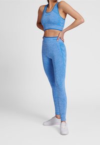 Světlomodré sportovní crop top a legíny vyrobené z texturované látky. Top má design s závodním výstřihem; legíny mají hladký povrch a detaily švů.