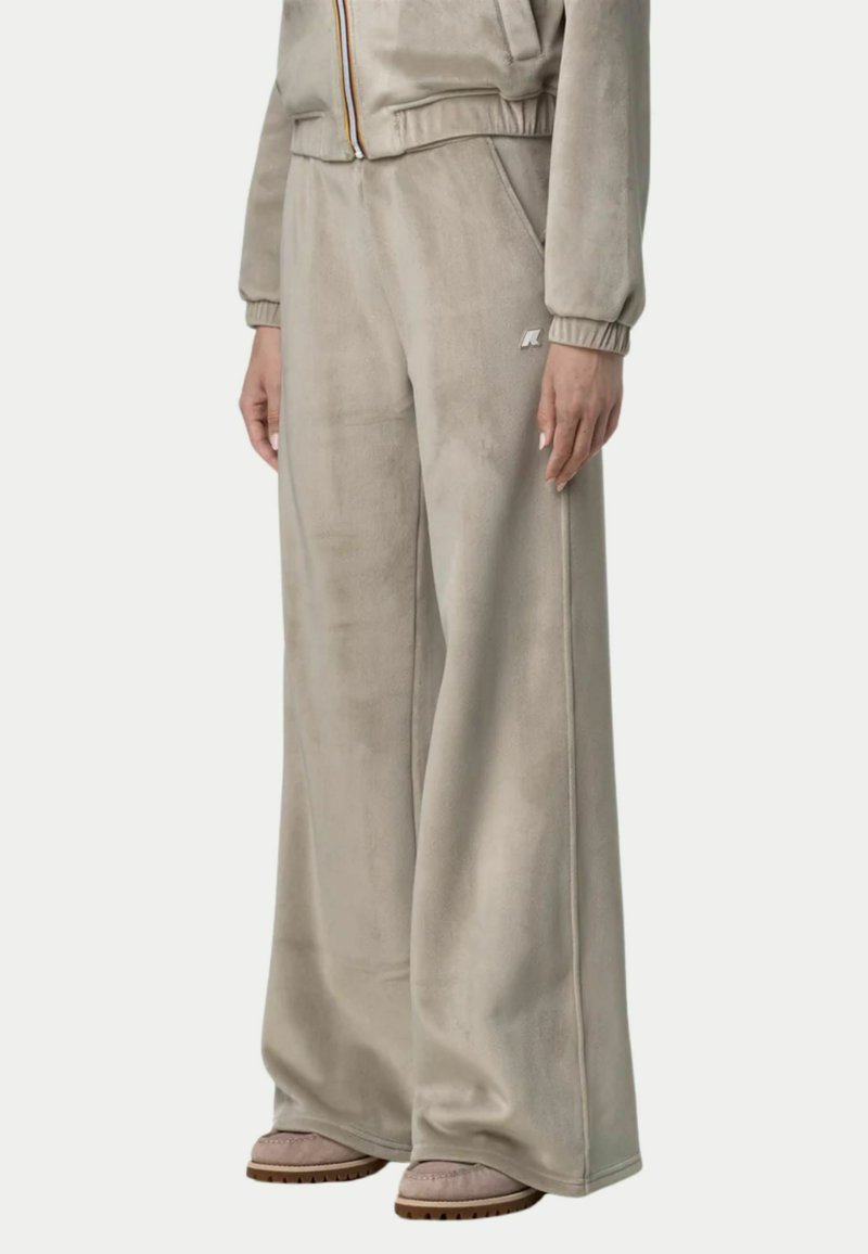 Pantaloni a gamba larga, in morbido beige, realizzati in tessuto peluche, con tasche laterali e un logo discreto sul davanti, abbinati a calzature coordinate.