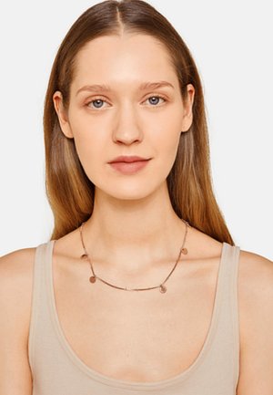 Metalen ketting met cirkelvormige hangeraccenten, met een dunne ketting en een roségouden afwerking, gedragen over een lichtbruine top.