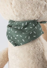 Beiger Plüsch-Spielzeug, das ein grünes Halstuch mit verstreuten weißen Punkten trägt. Das Halstuch ist ordentlich um den Hals des Spielzeugs gebunden.