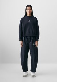 Navy blue sweatshirt with a round neckline and logo on the chest, paired with loose-fitting navy pants featuring side pockets and logo accents.