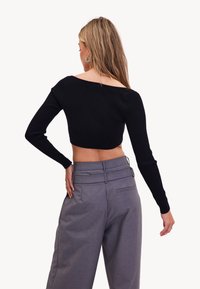 Zwarte ribgebreide cropped trui met lange mouwen, gecombineerd met hooggewaisted grijze broeken van een gestructureerde stof en een gladde tailleband.