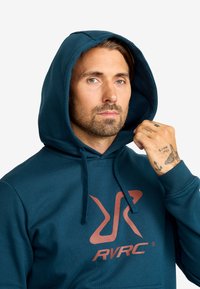 Hoodie i mörk teal med en framficka i kangaroo-stil. Har en stor orange RVRC-logotyp på bröstet och dragsnören för justerbar passform.