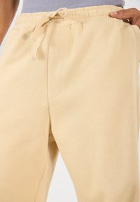 Beige sweatpants i mjukt material, med elastisk midjeband och snörning samt sidofickor, som visar en slät yta.