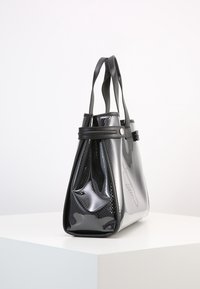 Černá taška typu tote vyrobená z hladkých a strukturovaných materiálů, s pevnou strukturou, dvojitými rukojeťmi a lesklým povrchem s jemným vzorem.