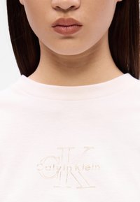 Ανοιχτό ροζ φούτερ με κεντημένο λογότυπο "Calvin Klein" σε κρεμ απόχρωση. Σχεδίαση με λαιμόκοψη και απαλή υφή με μινιμαλιστική αισθητική.