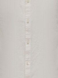 Gros plan sur le devant d'une chemise blanche à boutons avec des coutures visibles et quatre boutons transparents alignés verticalement.