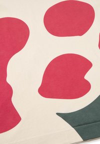 T-shirt with a cream base featuring large red organic shapes and a green accent, made of soft cotton with a smooth texture.