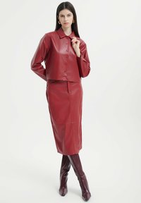 Rote Leder-Cropped-Jacke mit Knopfverschluss und langen Ärmeln, kombiniert mit einem passenden Bleistiftrock und knielangen spitzen Stiefeln.