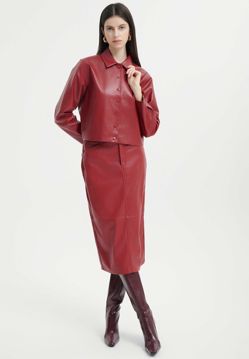 Rote Leder-Cropped-Jacke mit Knopfverschluss und langen Ärmeln, kombiniert mit einem passenden Bleistiftrock und knielangen spitzen Stiefeln.