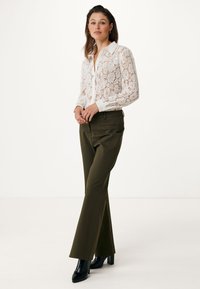Blusa bianca in pizzo con colletto, abbinata a pantaloni verde oliva a taglio slim. Stivali neri con tacco completano il look.