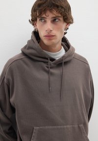 Felpa marrone con vestibilità rilassata, dotata di cappuccio con cordino, tasca a marsupio e tessuto testurizzato. Design semplice con un colore neutro.